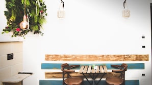 A dining area with a wooden table and chairs, a hanging plant, and a wall-mounted light fixture. - B&B BEL SALENTO SPECCHIA (Specchia)