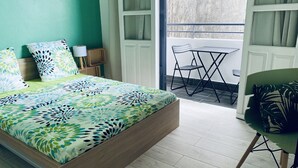 Een slaapkamer met een bed, een stoel, een klein tafeltje en uitzicht op het balkon.