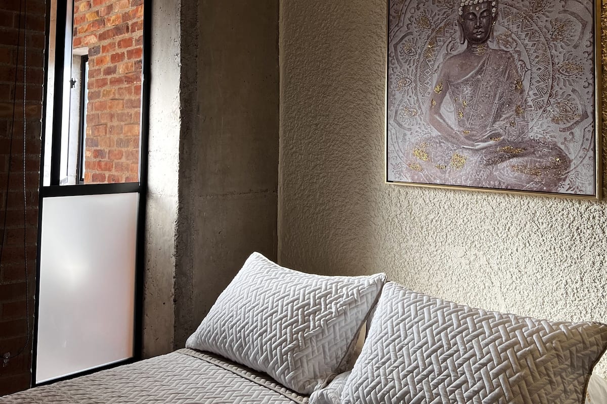 A bedroom with a bed, a ceiling fan, a window, and a Buddha painting on the wall.
