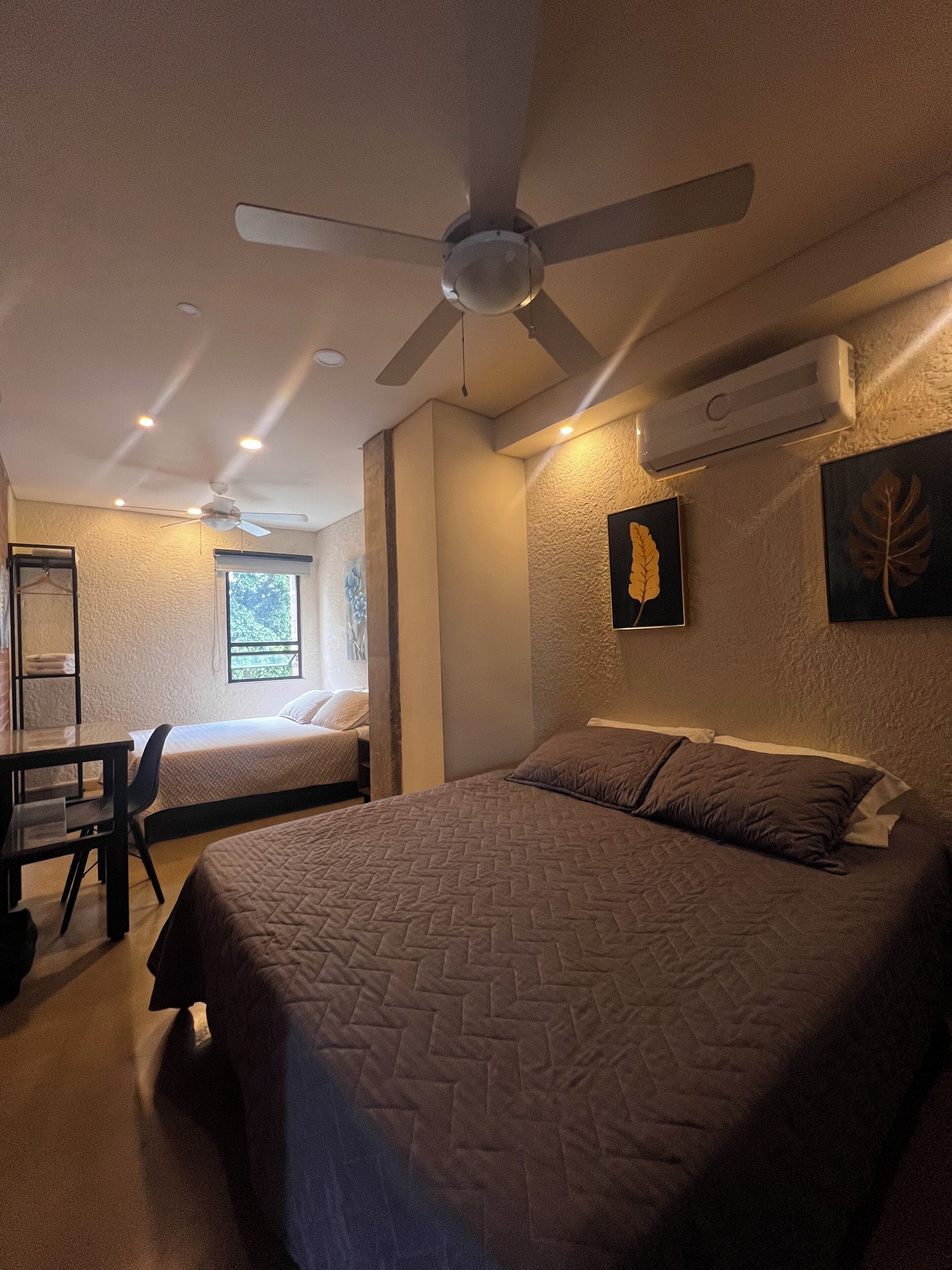 A bedroom with a bed, a desk, a chair, a ceiling fan, and an air conditioning unit.