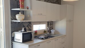 A compact kitchen with white cabinets, a microwave, a sink, and a window above the counter. - COZY AND ELEGANT COTTAGE WITH PENTHOUSE (Polignano a Mare)