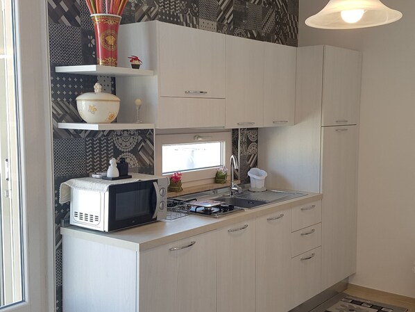 Una cocina compacta con armarios blancos, microondas, lavamanos y una ventana sobre la encimera.
