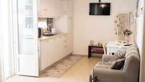 A compact kitchen with a dining area, a sofa, and a TV mounted on the wall. - COZY AND ELEGANT COTTAGE WITH PENTHOUSE (Polignano a Mare)