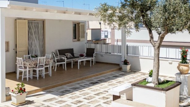 A covered outdoor patio with a seating area, a tree, and potted plants. - COZY AND ELEGANT COTTAGE WITH PENTHOUSE (Polignano a Mare)