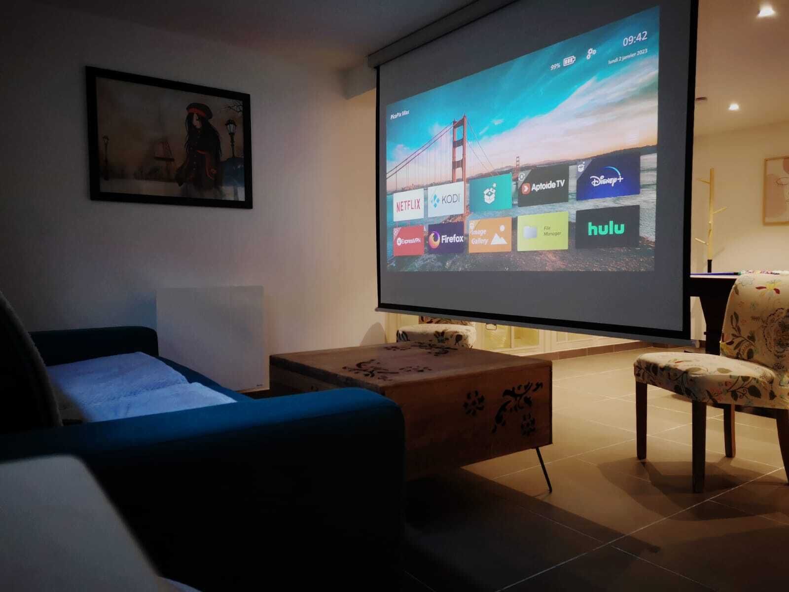 A living room with a large screen displaying streaming services, a sofa, a coffee table, and a chair.
