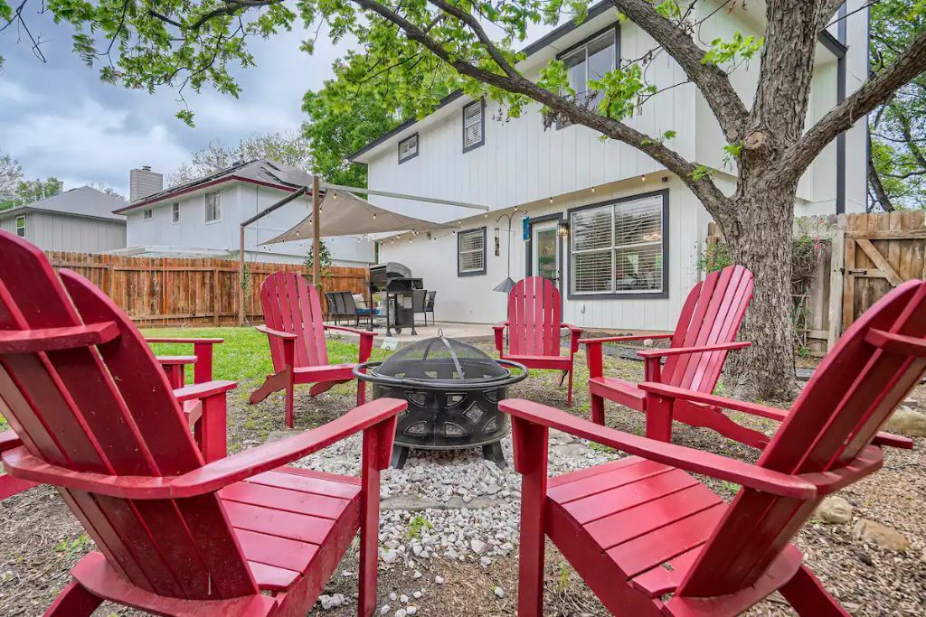 A backyard with red Adirondack chairs, a fire pit, and a barbecue grill.