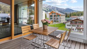 Ein Balkon mit Holztisch und Stühlen, einem Blumenstrauß und Blick auf eine gebirgige Landschaft.