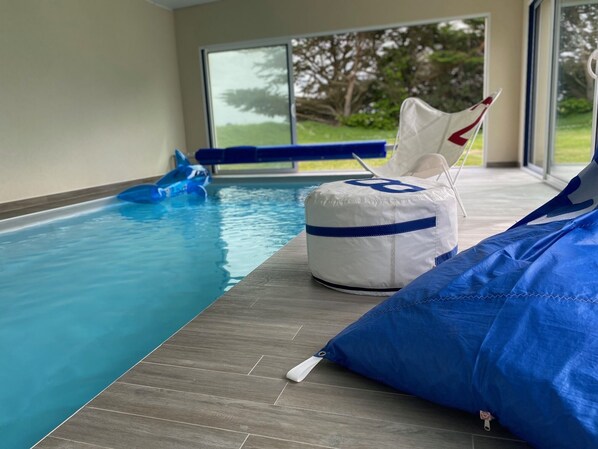 An indoor swimming pool with a blue inflatable shark, a white and blue floating seat, and a blue lounge chair.
