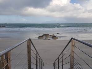 A beach with a staircase leading to the shore, surrounded by rocks and waves.