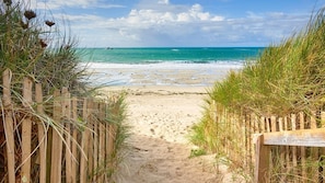 A sandy beach path leading to the ocean, surrounded by wooden fences and tall grasses.