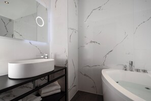 Un baño moderno con un lavamanos blanco, un espejo grande y una bañera independiente.