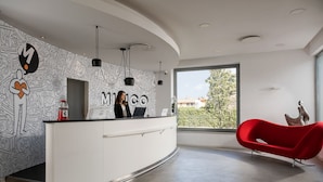 Un área de recepción moderna con un escritorio blanco, arte mural en blanco y negro, y una silla roja.