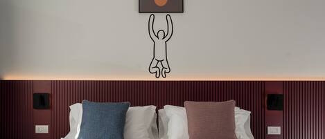 A hotel room with a bed, pillows, a wall-mounted artwork, and a red textured wall.