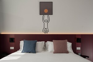 Una camera d'hotel con un letto, cuscini, un'opera d'arte appesa al muro e una parete rossa con texture.