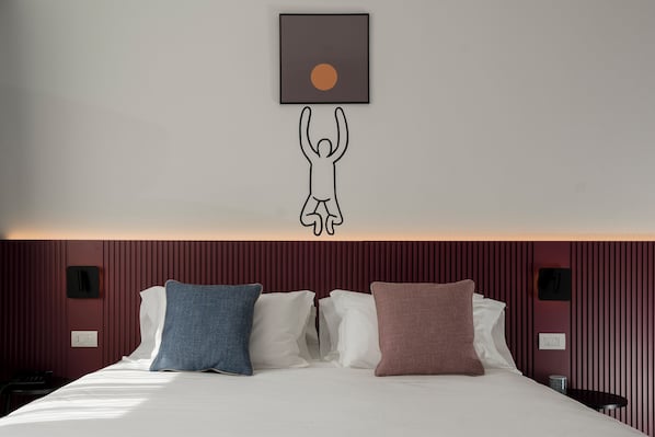 Une chambre d’hôtel avec un lit, des oreillers, une œuvre d’art accrochée au mur et un mur rouge à texture.