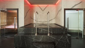 Un moderno vestíbulo con pisos de mármol, una escalera central, puertas de cristal y techo iluminado en rojo.