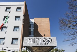 Een hotelschild met de naam 'MITICO HOTEL' en een vlaggenmast met een vlag.