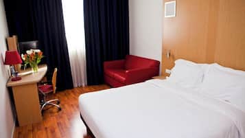 Una habitación de hotel con un escritorio de madera, una silla roja, una cama con ropa blanca y un televisor sobre el escritorio.