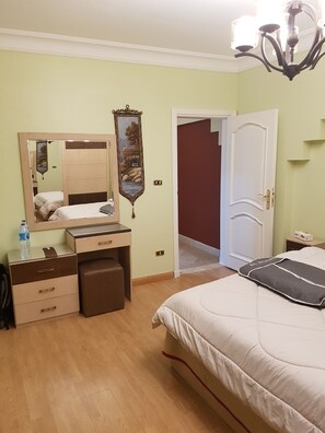 A bedroom with a bed, a dresser, a mirror, a nightstand, and a door leading to another room.