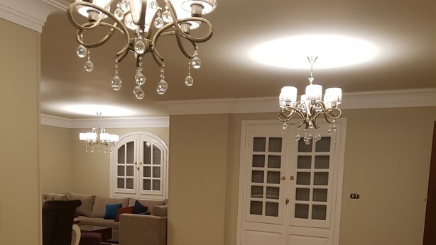 Un salón amplio con candelabro, un conjunto de sofás y una puerta con paneles de vidrio.