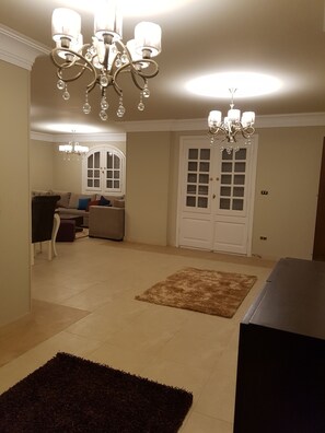 A spacious living room with a chandelier, a sofa set, and a door with glass panels.