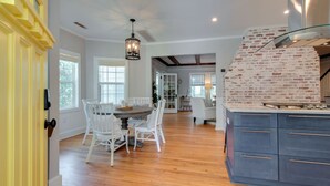 A spacious kitchen with a brick accent wall, wooden flooring, and a dining area with white chairs and a round table. - PREMIER Landmark Home Located in Old Town Bluffton  (Bluffton)