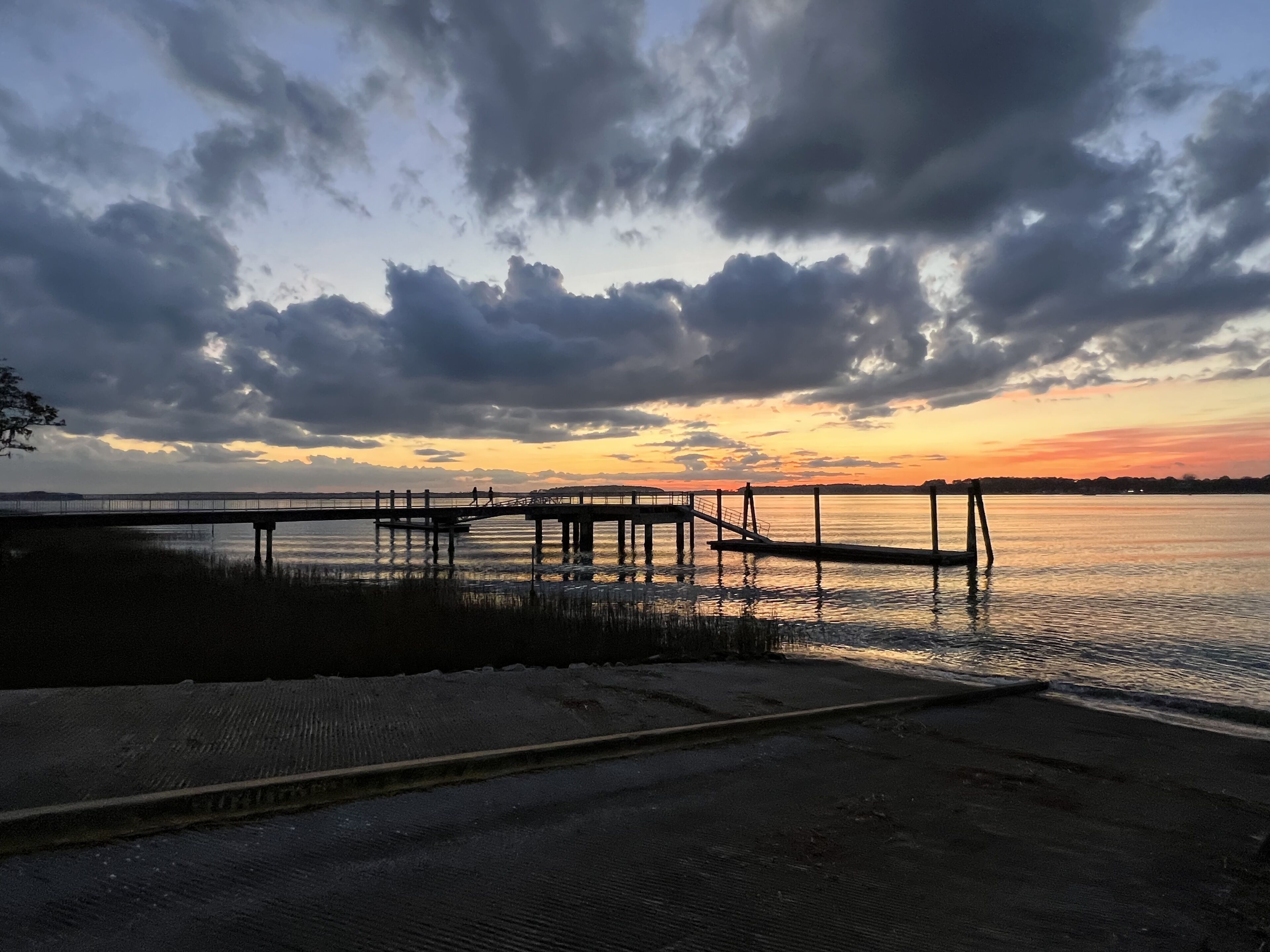 Un muelle se adentra en el agua con un atardecer de fondo.