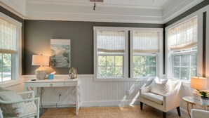 A room with a white desk, a chair, a lamp, and a large window with a view of greenery. - PREMIER Landmark Home Located in Old Town Bluffton  (Bluffton)