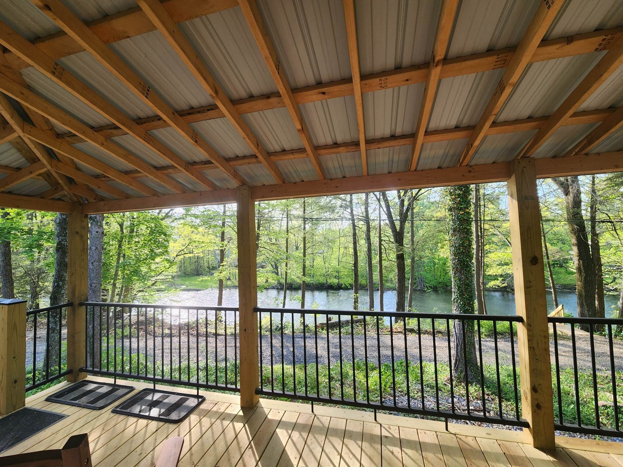 A covered outdoor deck with a view of a forest and a river.