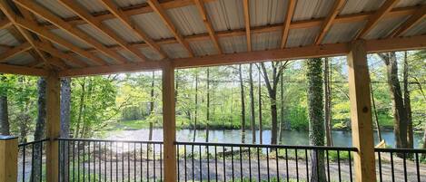 A covered outdoor deck with a view of a forest and a river.
