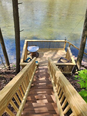 A wooden deck with a table and chairs, leading to a body of water. - Fly Away Cabin: Relax and enjoy the creek views and sounds. (Millmont)