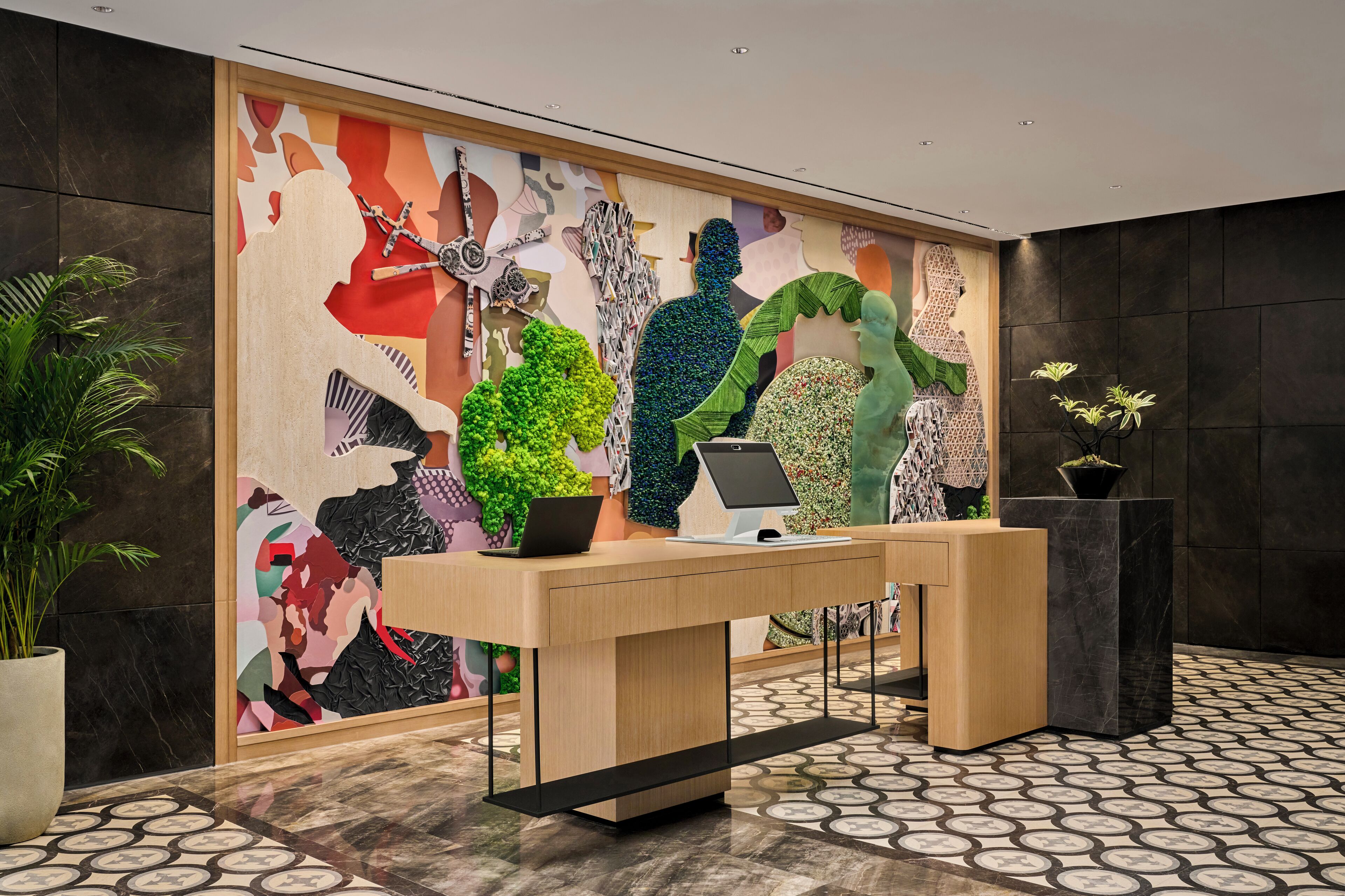 A reception desk with a modern design, a colorful abstract mural on the wall, and potted plants.