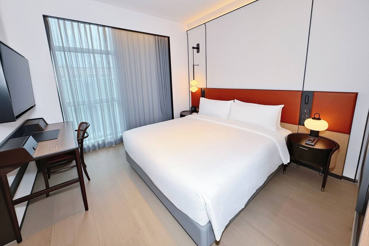 A hotel room with a large bed, a desk with a chair, a TV, and a window with curtains.