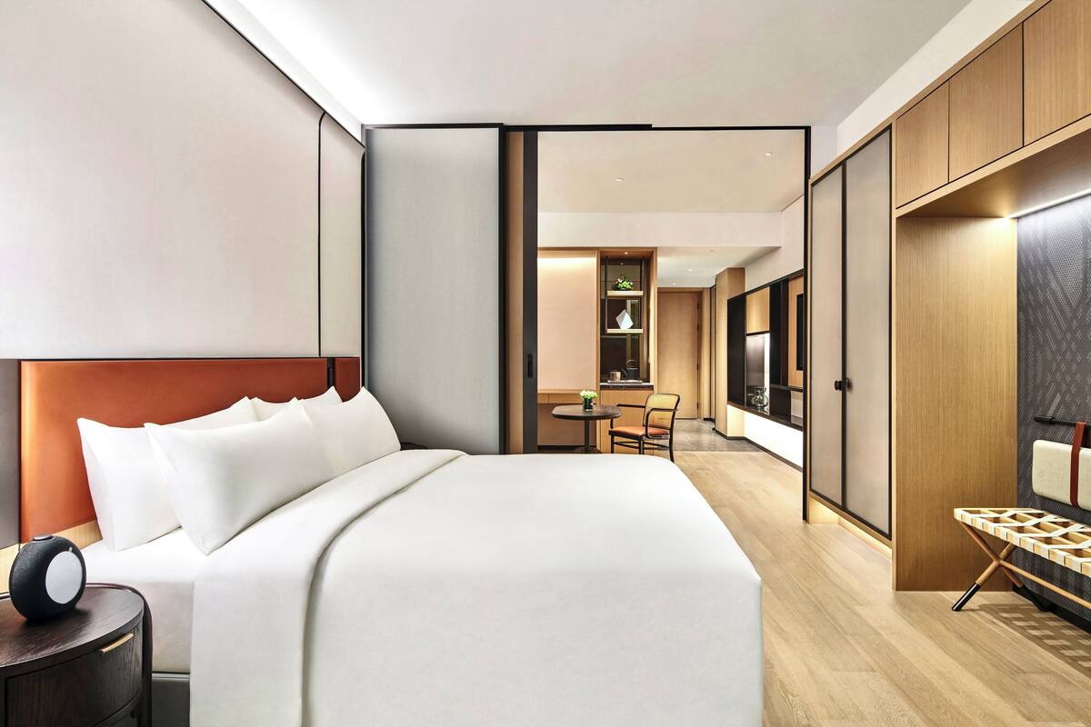 A modern hotel room with a large bed, a bedside table, a desk, and a wardrobe.