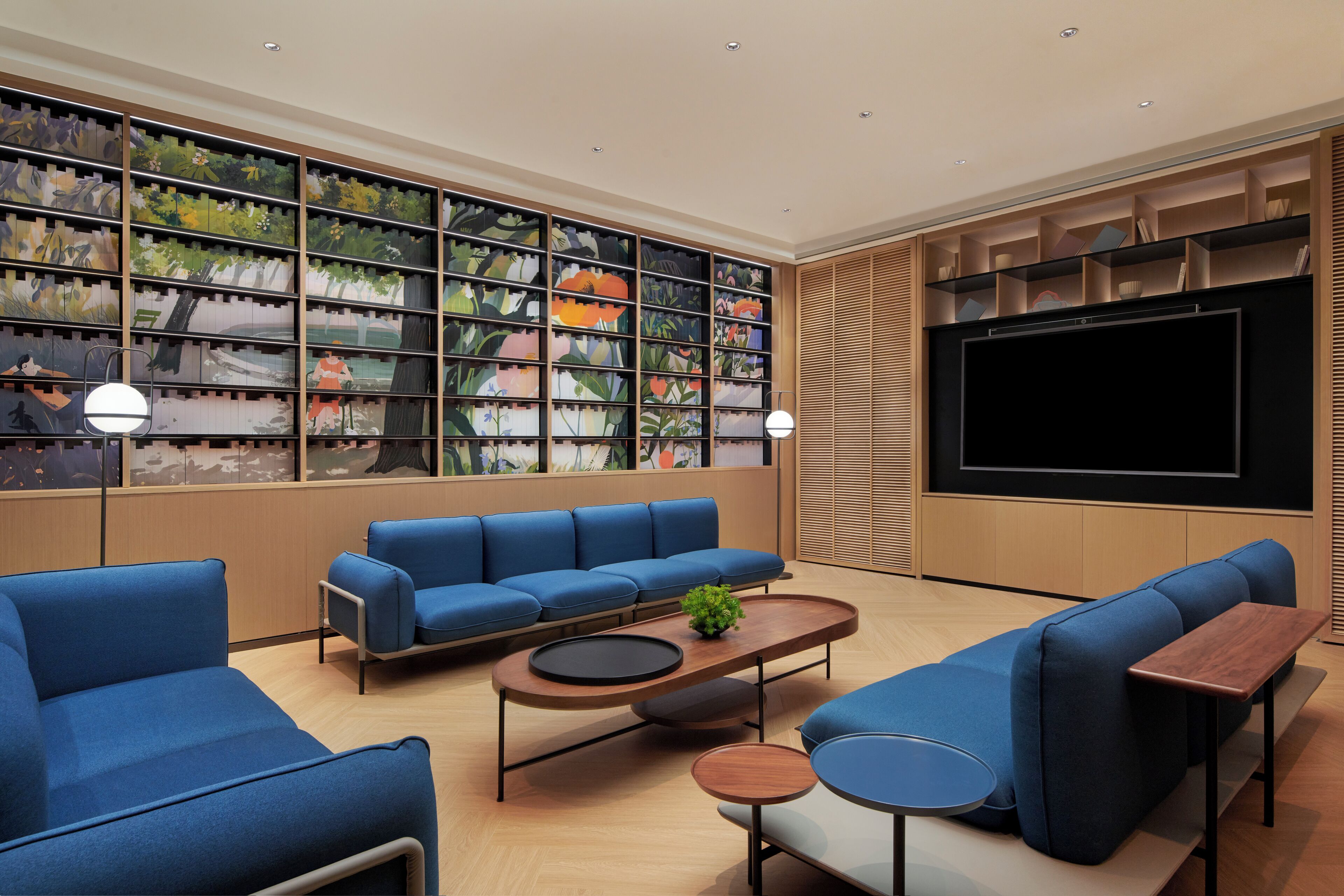 A modern living room with blue sofas, a coffee table, and a bookshelf filled with colorful artwork.