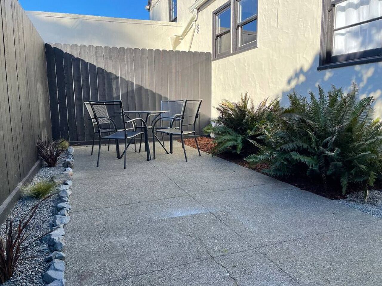 Un patio con una mesa, sillas, un cerco de madera y algunas plantas.