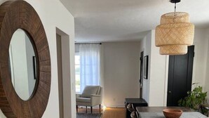 Un comedor moderno con una mesa de madera, sillas y una lámpara colgante de fibras naturales. Se ve un espejo grande en la pared, y una silla al fondo.