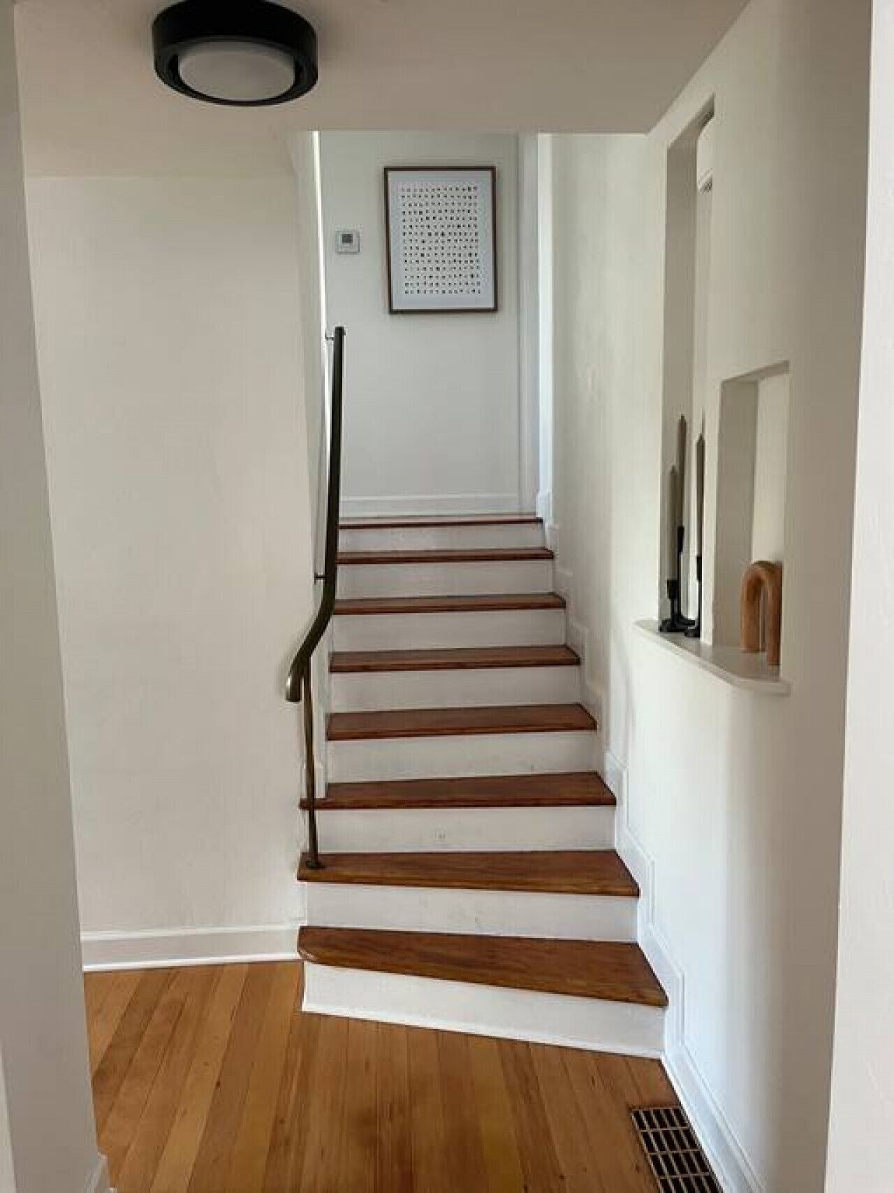 A staircase with wooden steps and a black handrail, leading to a landing with a framed picture on the wall.