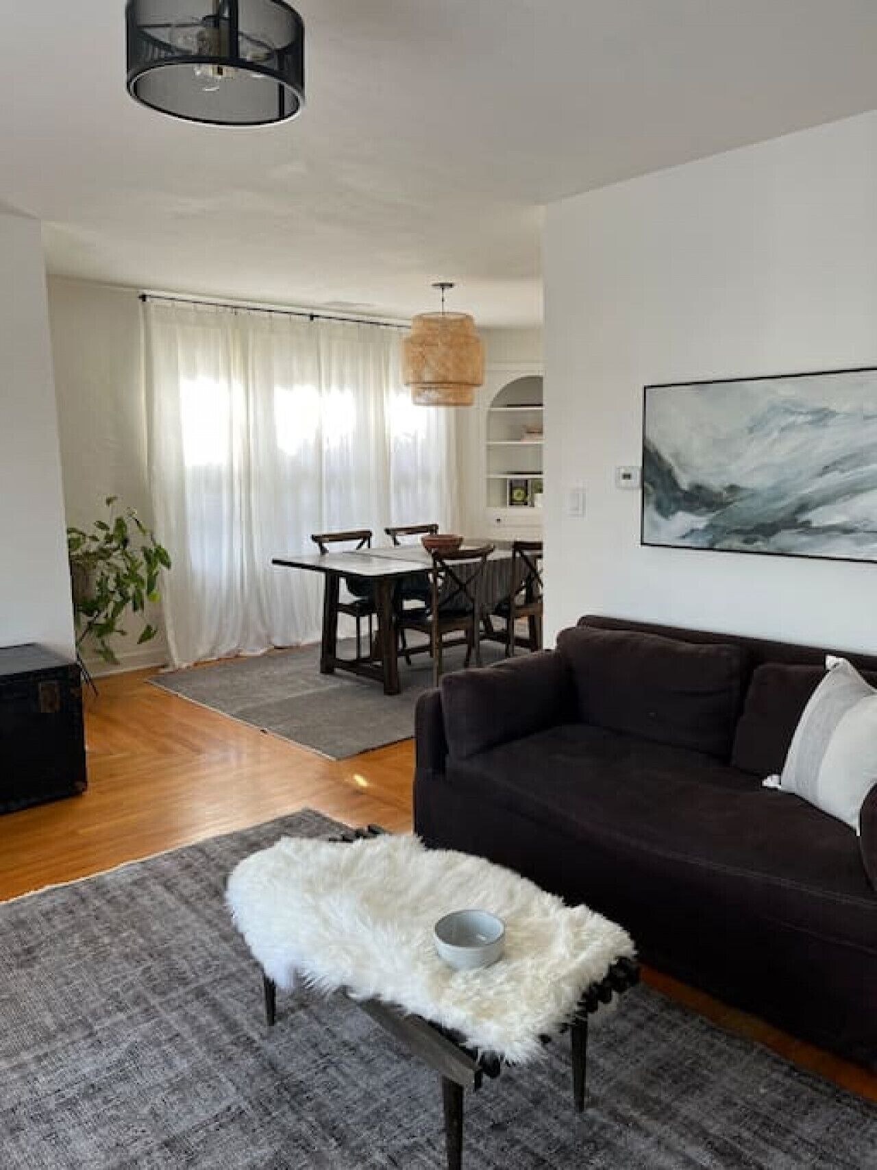 Ein Wohnzimmer mit einem dunkelbraunen Sofa, einem weißen, flauschigen Teppich und einem Essbereich mit Tisch und Stühlen.