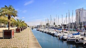 A marina with boats docked along a cobblestone waterfront, palm trees lining the path, and buildings in the background. - L'Aparté ★ HYPER CENTRE ★ LUMINEUX ★ (Lorient)