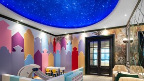 Ein Kinderspielbereich mit Sternenhimmel, farbenfrohen geometrischen Wandbildern und einer Rutsche.