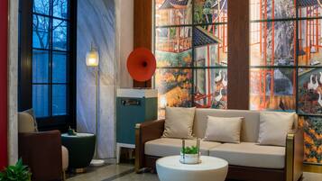 A modern interior with a sofa, a round coffee table, a floor lamp, and a large window with a view of trees.
