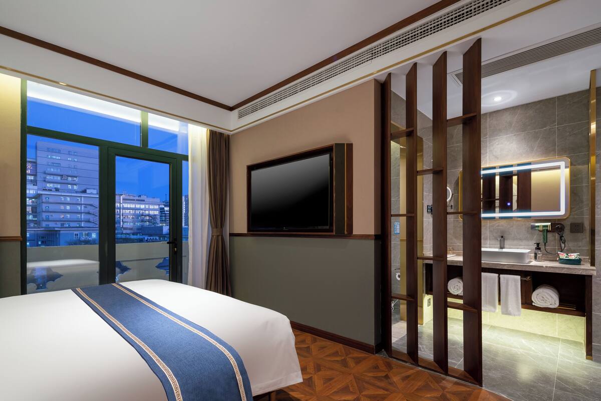 Una camera d'albergo con un letto, una televisione, un bagno con uno specchio e vista sui palazzi.