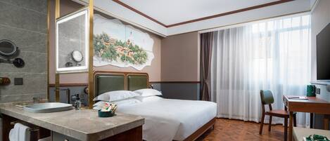 A hotel room with a bed, a desk, a chair, a bathroom with a sink and mirror, and a large window with curtains.