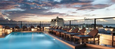 A rooftop pool area with lounge chairs and a view of the city skyline.