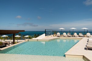 Zona de piscina con sillones y sombrillas, con vista a una playa y al océano.