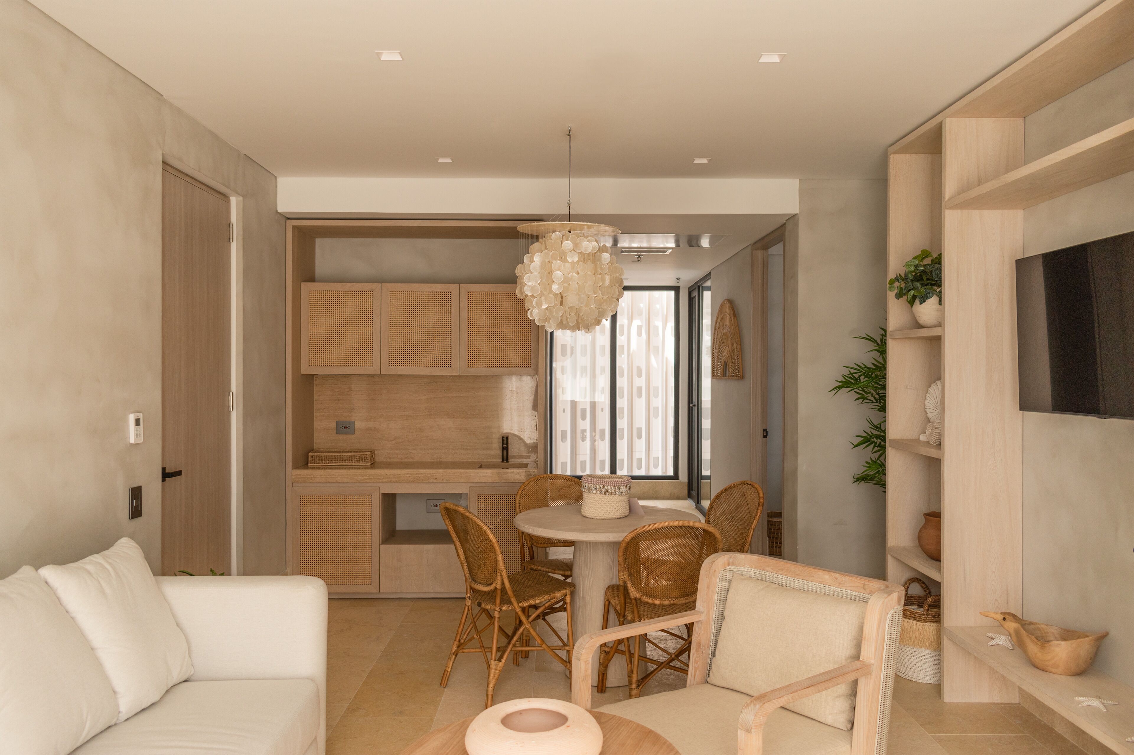 A modern living room with a white sofa, wicker chairs, a round dining table, and a hanging light fixture.