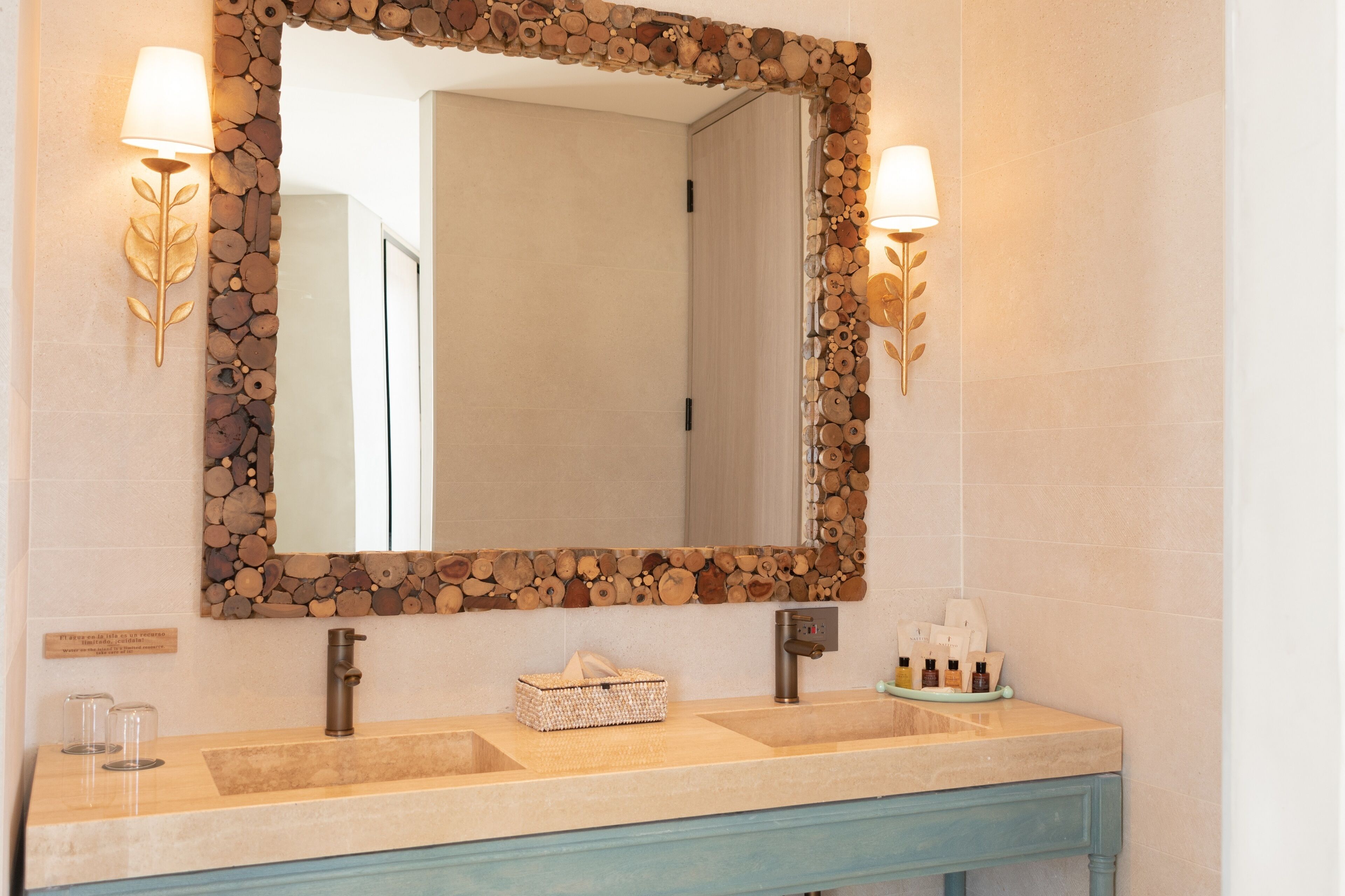 A bathroom with a wooden-framed mirror, two wall-mounted lights, a sink with a towel, and toiletries.