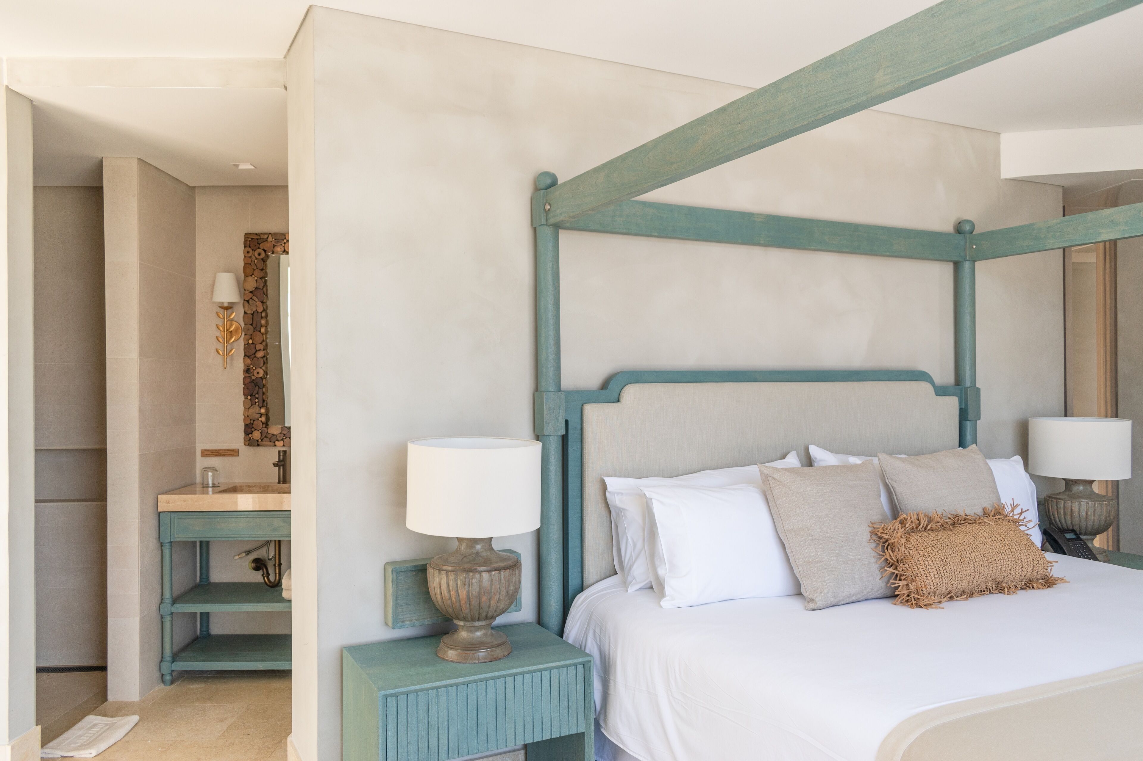Un dormitorio con cama con dosel, una mesita de noche con lámpara, un tocador con espejo y una estantería en la pared.