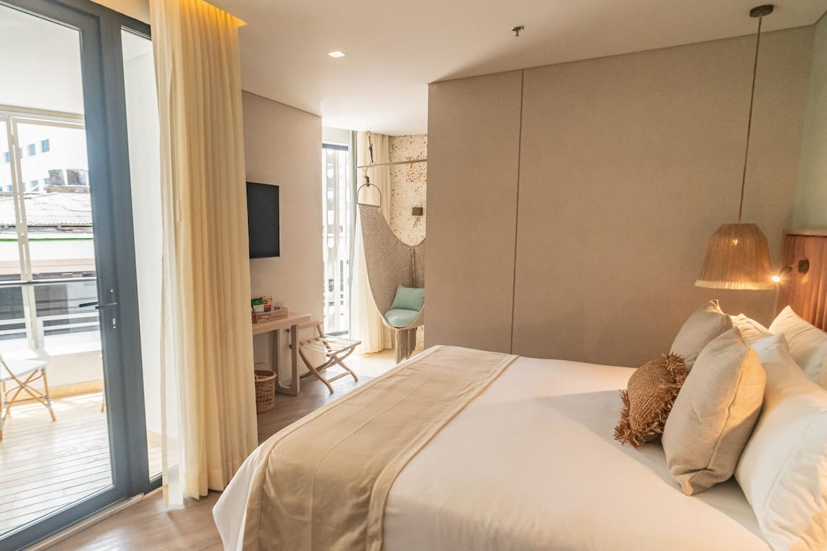 Ein Hotelzimmer mit einem großen Bett, einem Schreibtisch und einem Stuhl. Ein Balkon bietet Blick ins Freie.